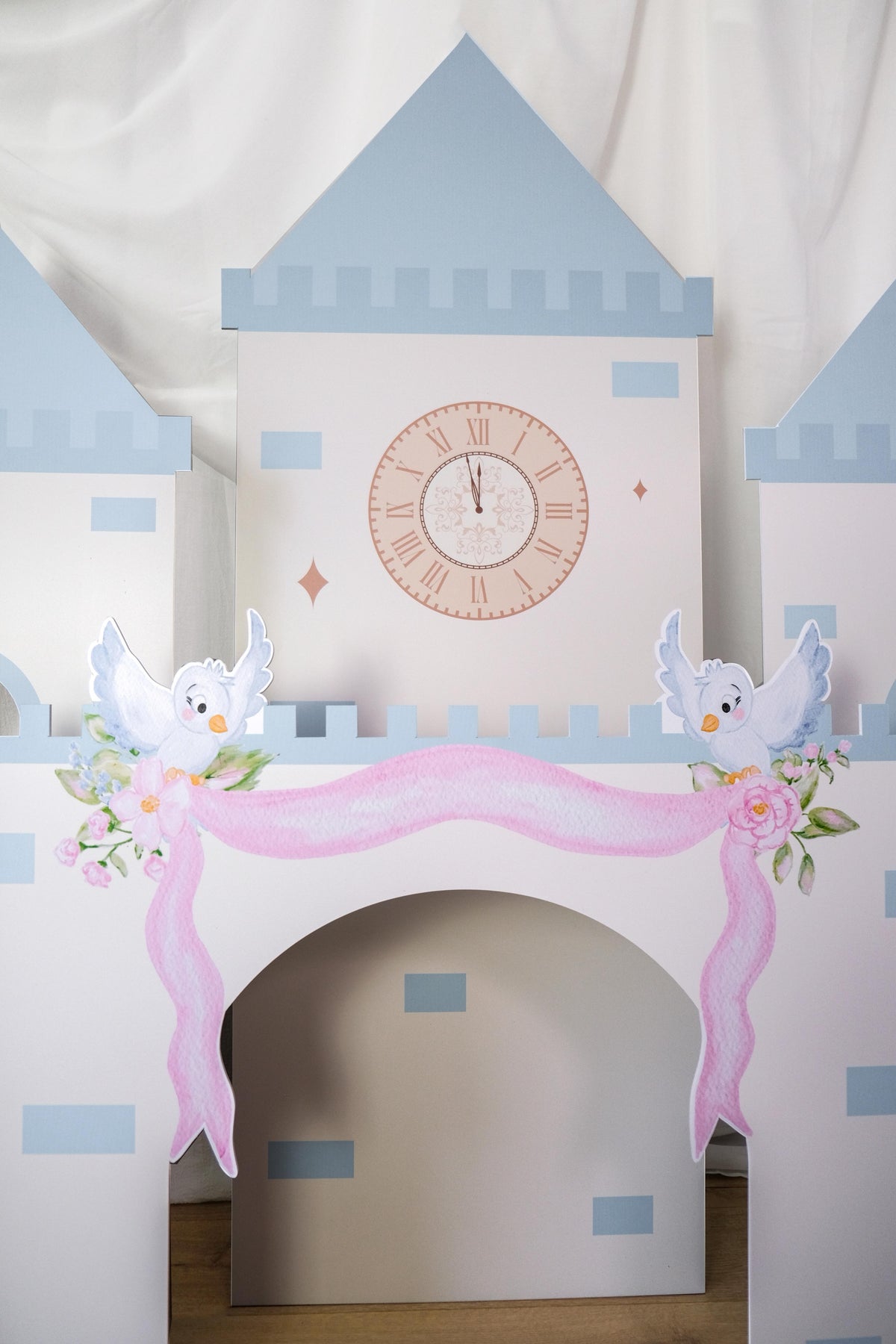 Close-up of Midnight Castle clock tower with blue turret, clock face, swan decorations, pink drapes, and roses around arched doorway waterproof foamex castle party prop