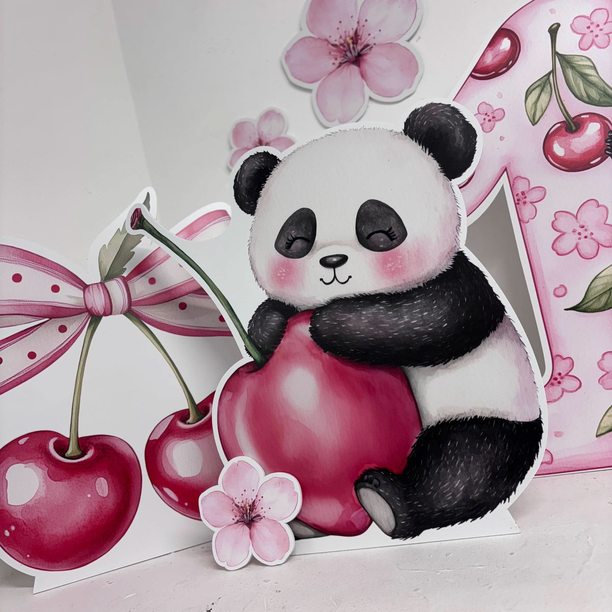 Close-up of Mini Cherry First Birthday waterproof foamex cutouts showing panda holding cherry with cherry blossoms, pink bow, and cherry decorations