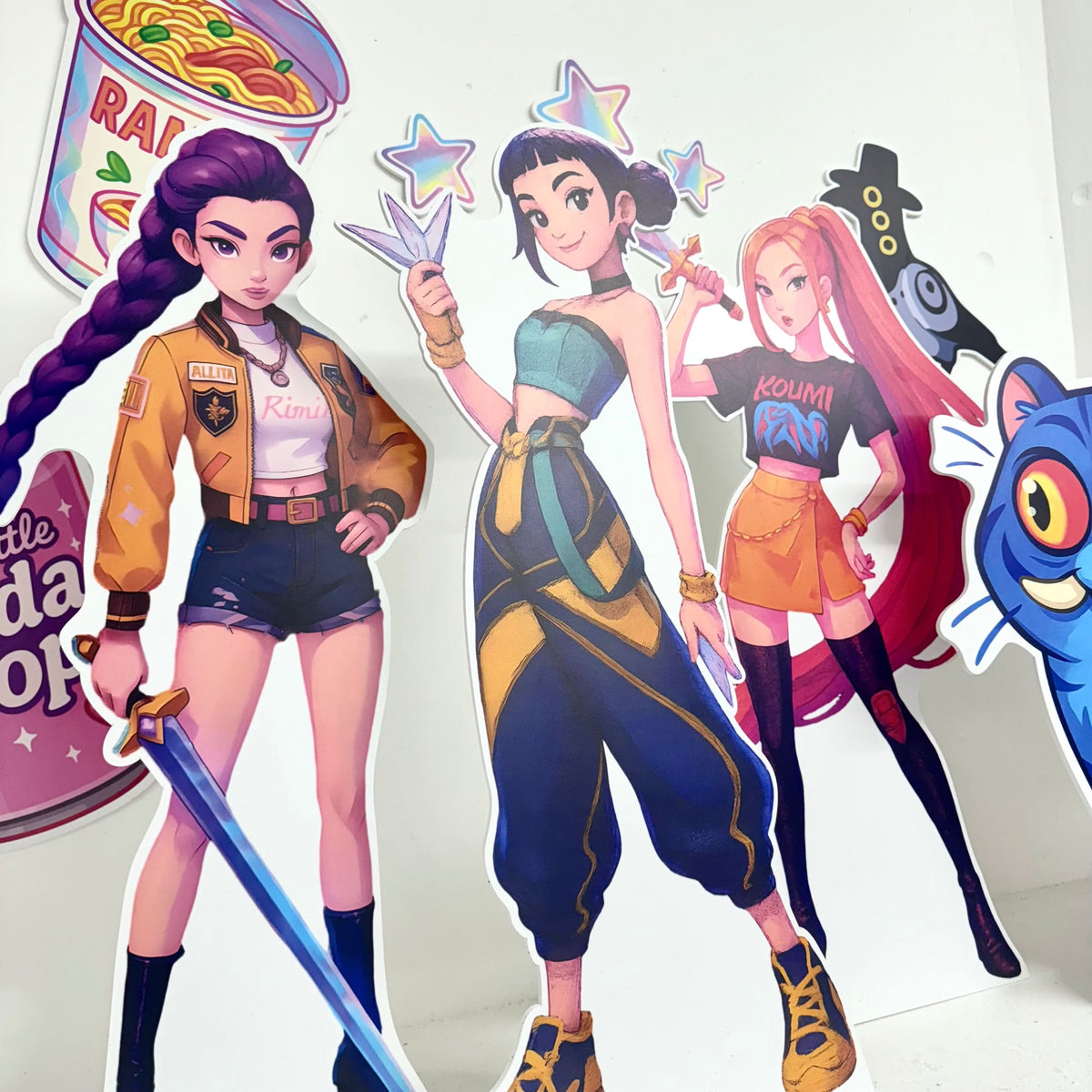 Close-up of Mini Girl Demon Hunters waterproof foamex cutouts showing purple-haired girl with sword, dark-haired girl warrior, and pink-haired girl with blue tiger creature