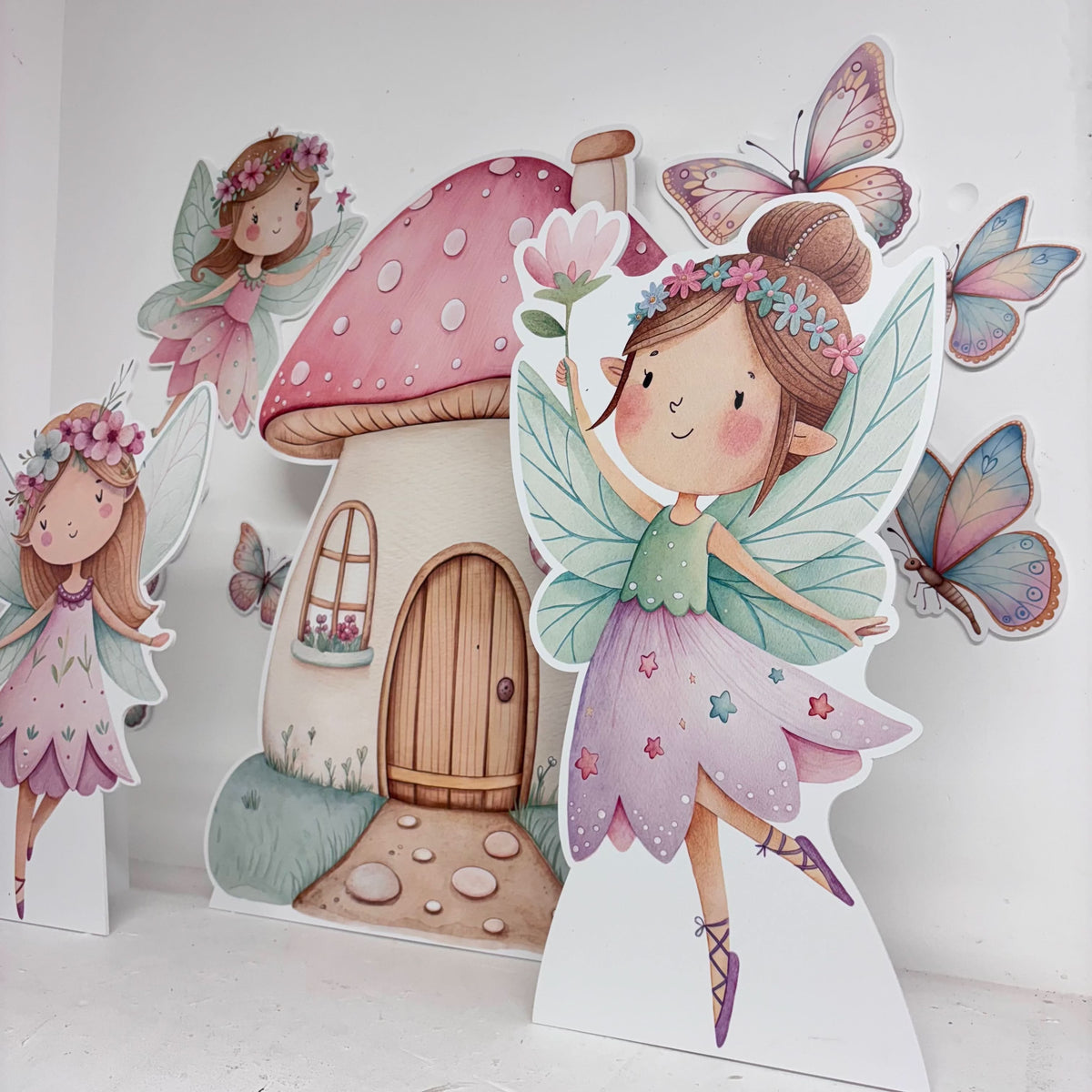 Close-up of Mini Garden Fairies waterproof foamex cutouts showing fairy girl with wings, mushroom house, butterflies, and enchanted garden party decorations