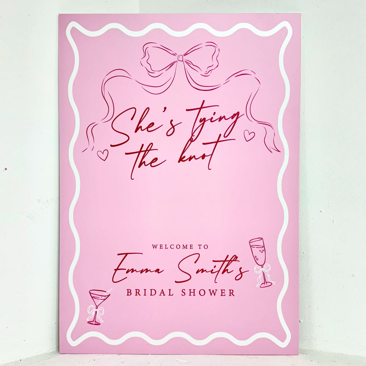 She's Tying the Knot bridal shower easel sign in pink with bow illustration, cocktail glass, hearts, and personalised name on a fun retro-style design