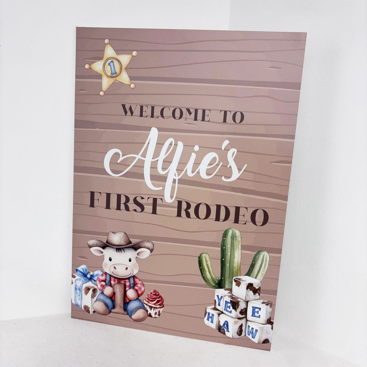 Close-up of My First Rodeo personalised 1st birthday welcome sign with cowboy character, sheriff badge, cactus and Yee Haw blocks on wooden-effect waterproof foamex board