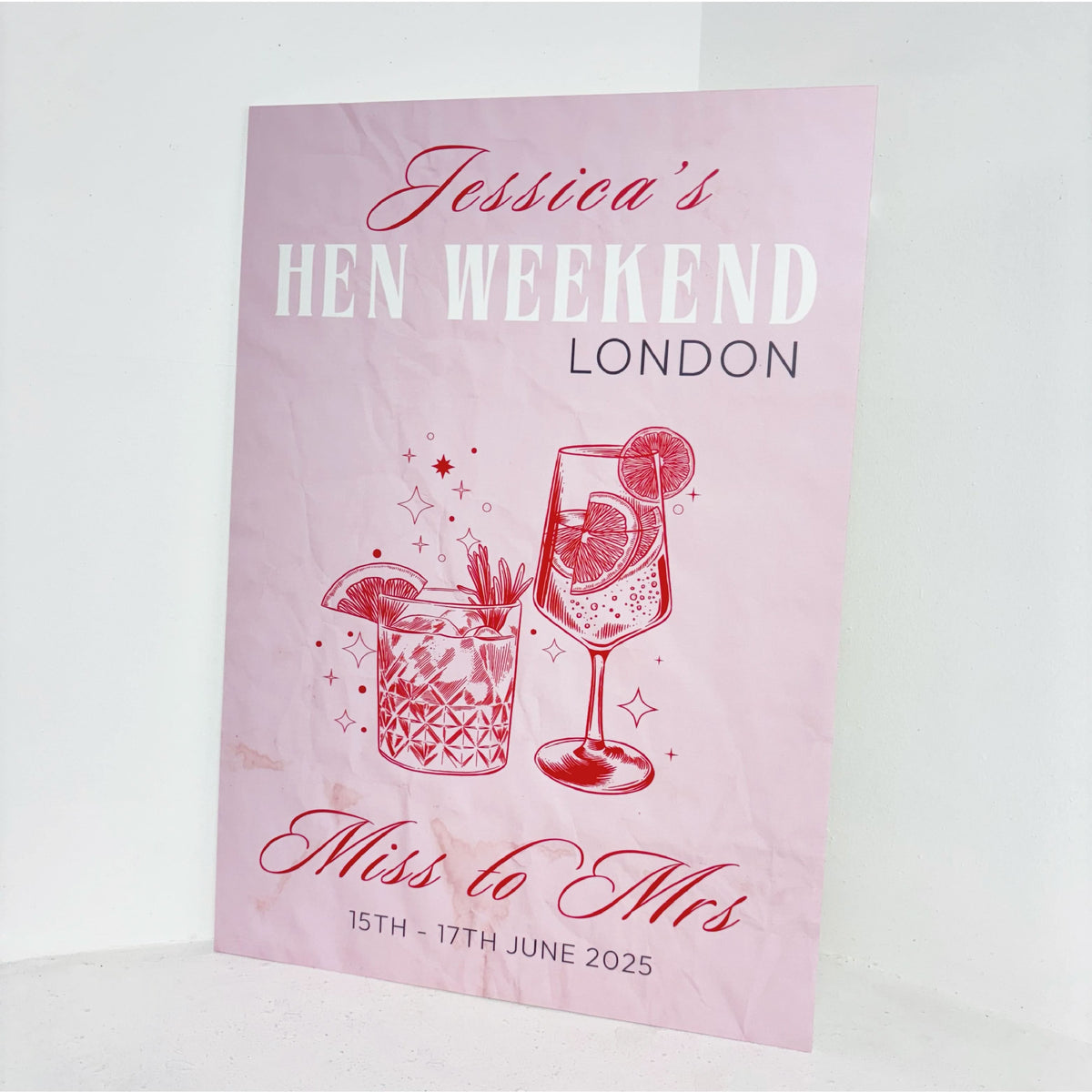 Angled view of Hen Weekend personalised hen party welcome sign on waterproof foamex board with pink background, cocktail glasses, and Miss to Mrs design