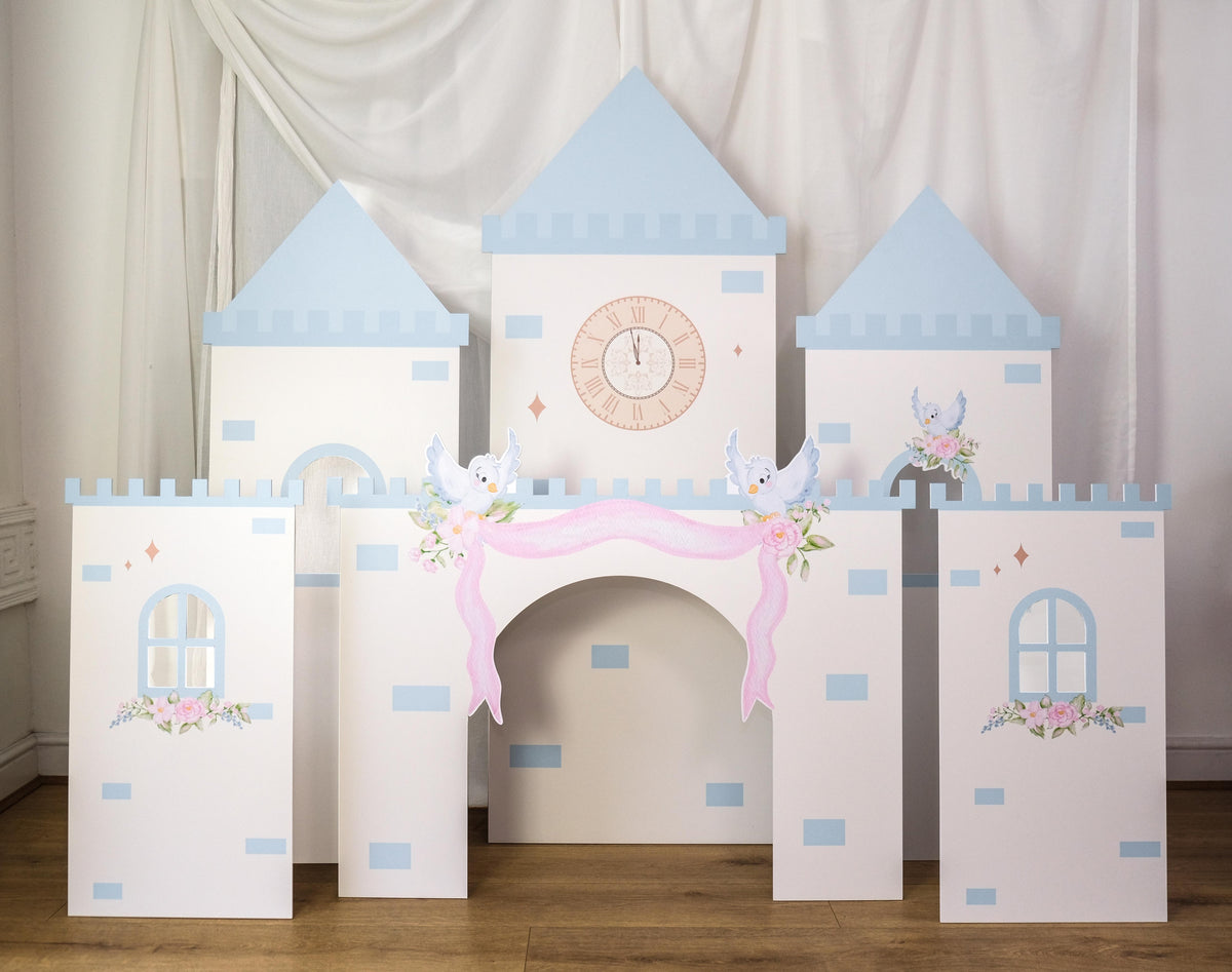 Midnight Castle waterproof foamex castle set featuring blue and white clock tower, side towers with arched windows, front towers, pink drapes, roses, and swan decorations party prop