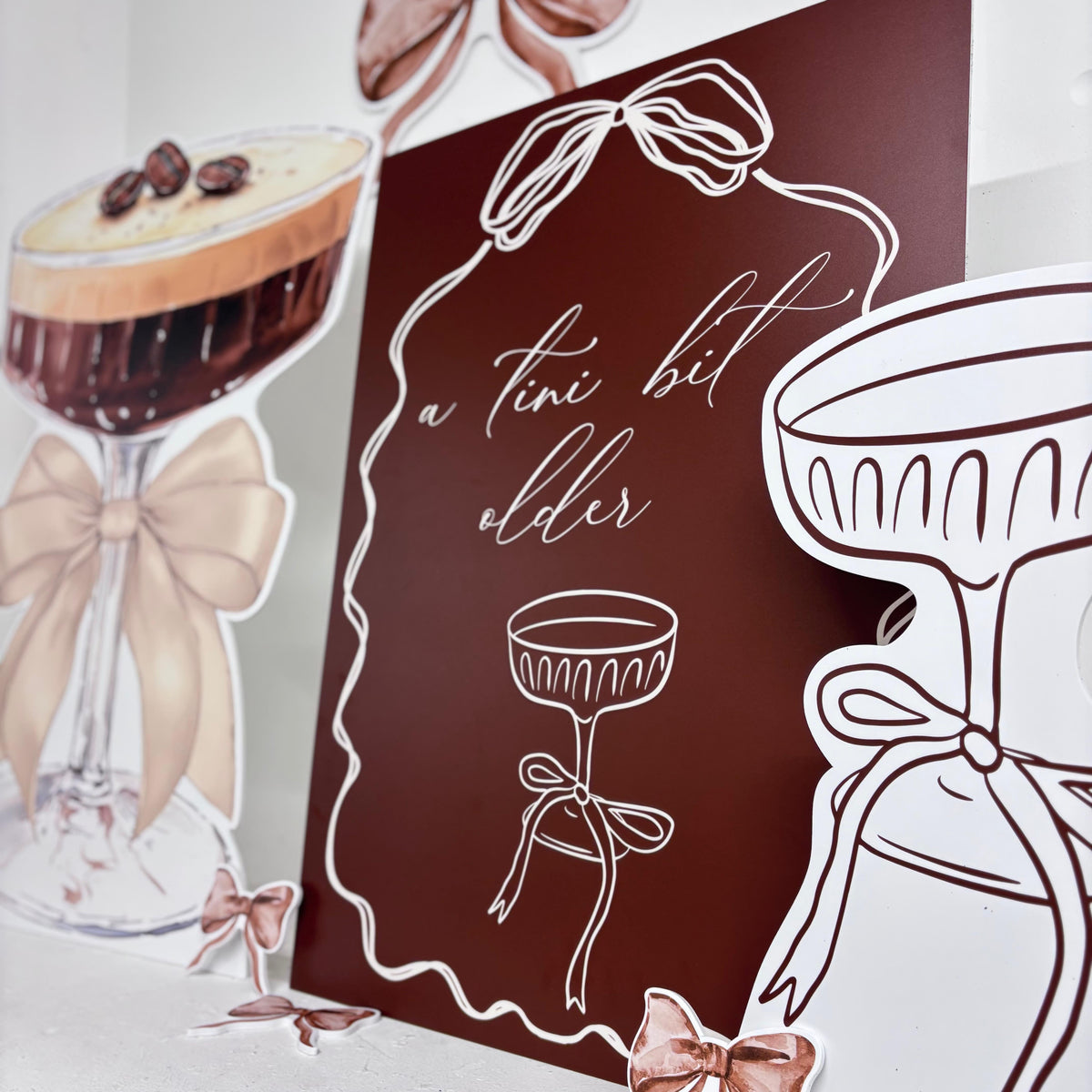 Close-up of Mini Tini Bit Older waterproof foamex cutouts showing a tini bit older sign, espresso martini, cocktail glass, bows, and birthday party decorations