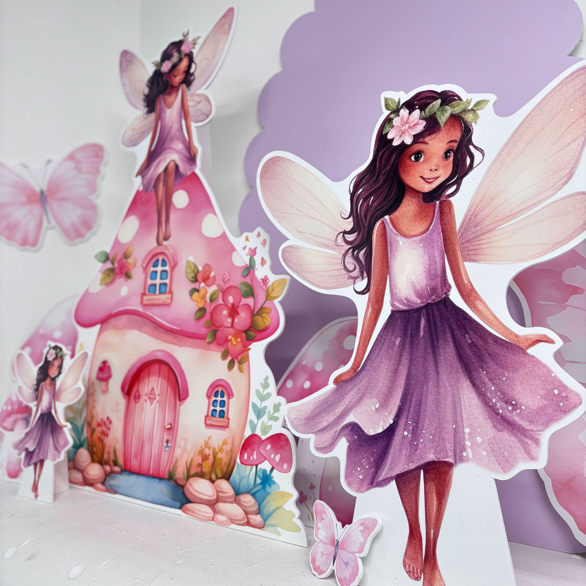 Close-up of Pastel Purple Fairies waterproof foamex cutouts showing fairy with flower crown and wings next to pink fairy house with butterflies and mushroom decorations