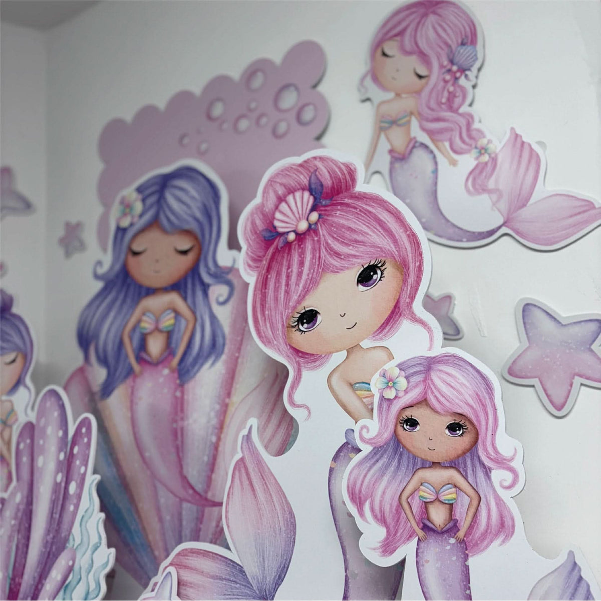 Close-up of Dreamy Mermaids waterproof foamex cutouts showing pink and purple haired mermaids with shell accessories and scalloped sail board party decorations