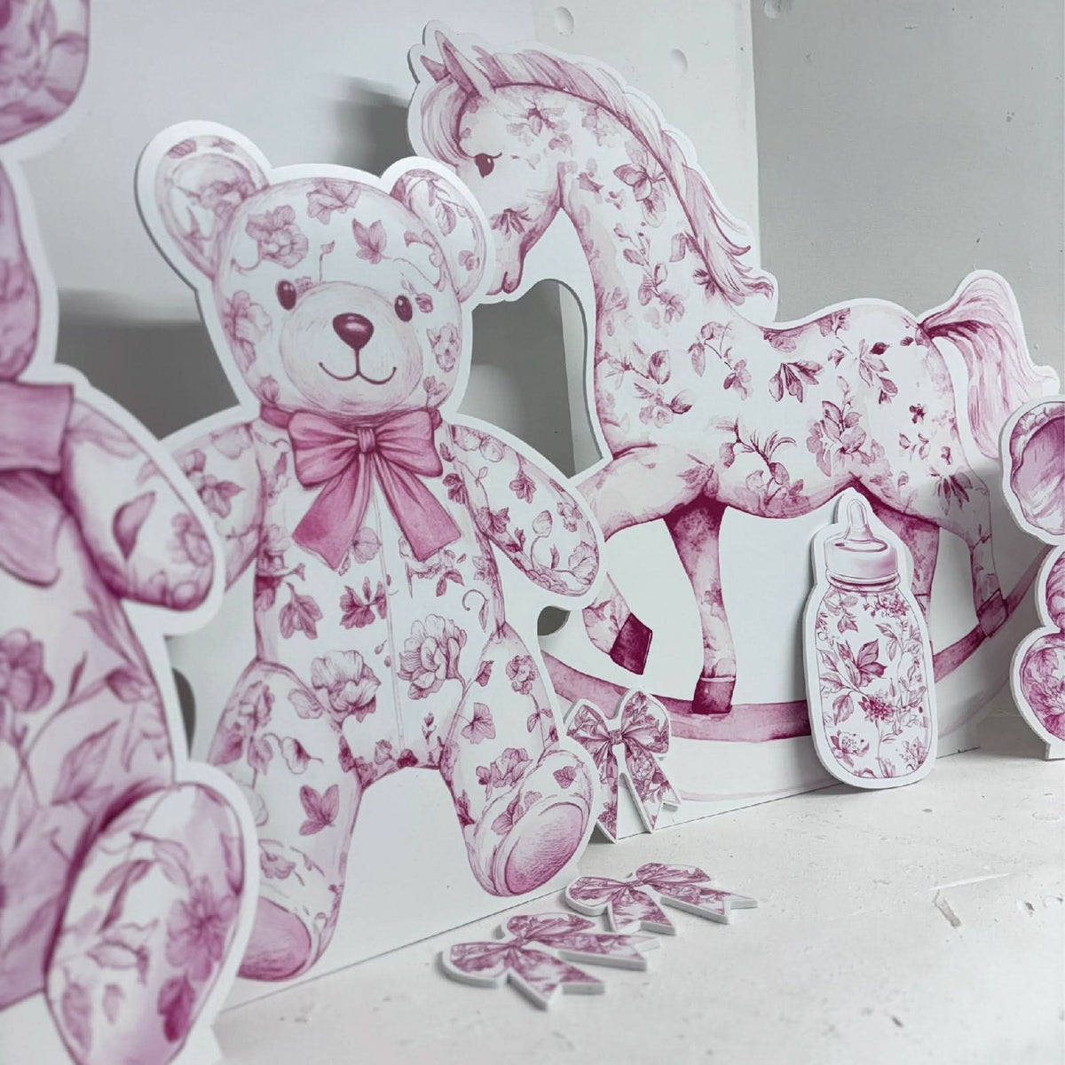 Close-up of Pink Baby Set waterproof foamex cutouts showing pink floral teddy bear, rocking horse, baby bottle, booties, and butterfly baby shower party decorations