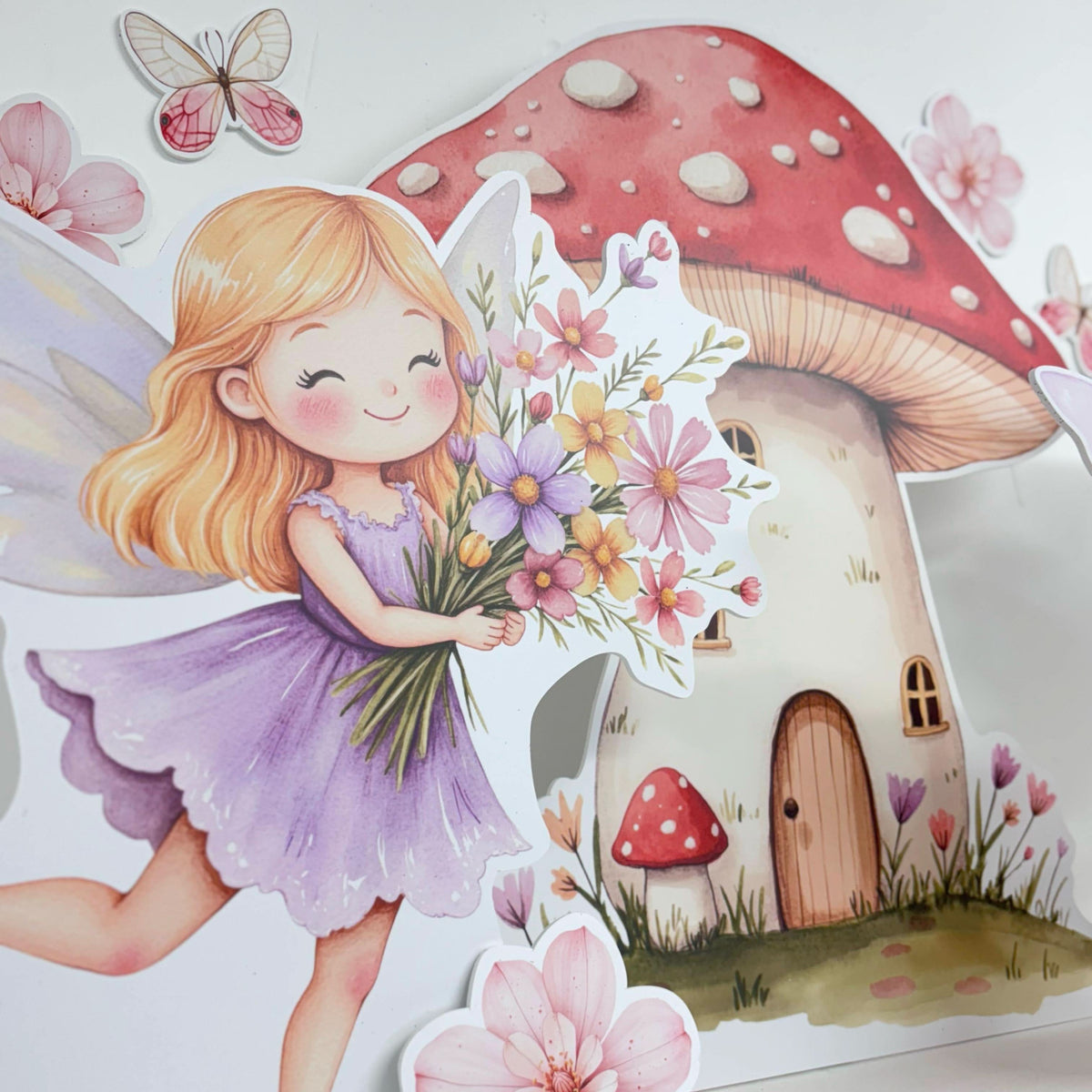 Close-up of Mini Spring Fairies waterproof foamex cutouts showing flower fairy in purple dress holding bouquet next to mushroom house with butterfly and pink blossom decorations