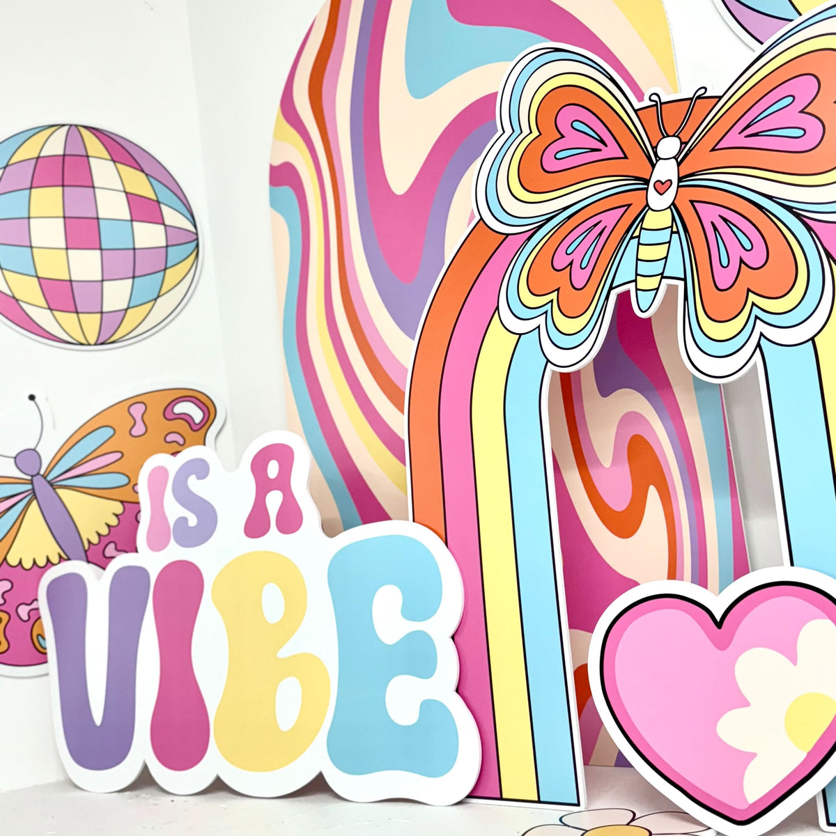 Close-up of What a Vibe Bundle waterproof foamex cutouts showing retro butterfly sailboard, Is a Vibe sign, swirl sailboard, disco ball, and pink heart flower party decorations