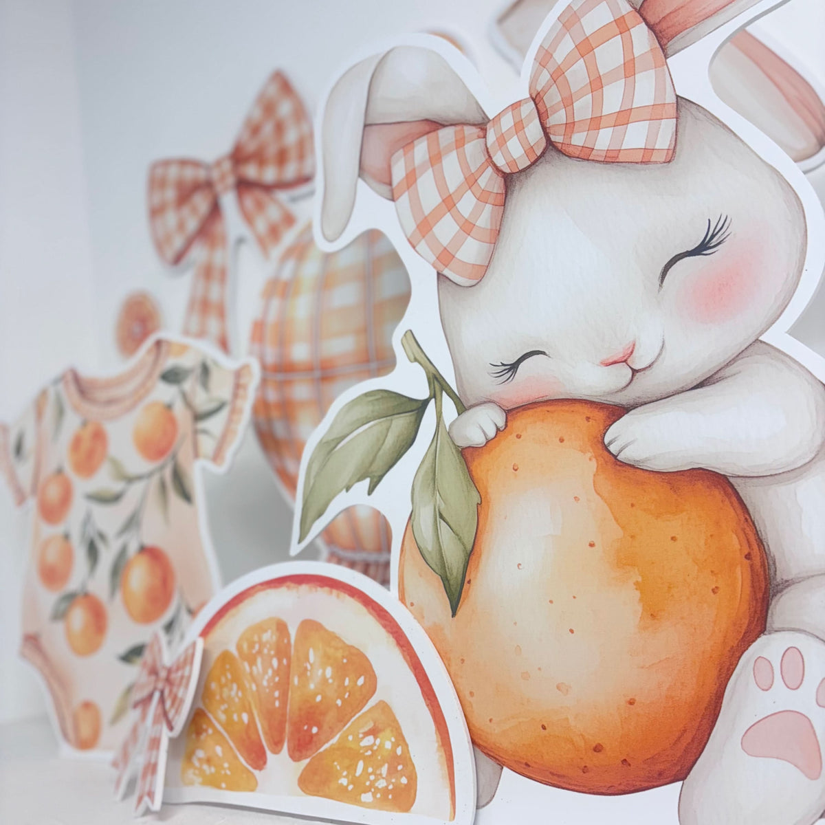 Close-up of Mini Our Little Clementine waterproof foamex cutouts showing bunny with gingham bow holding a clementine, orange slices and baby romper