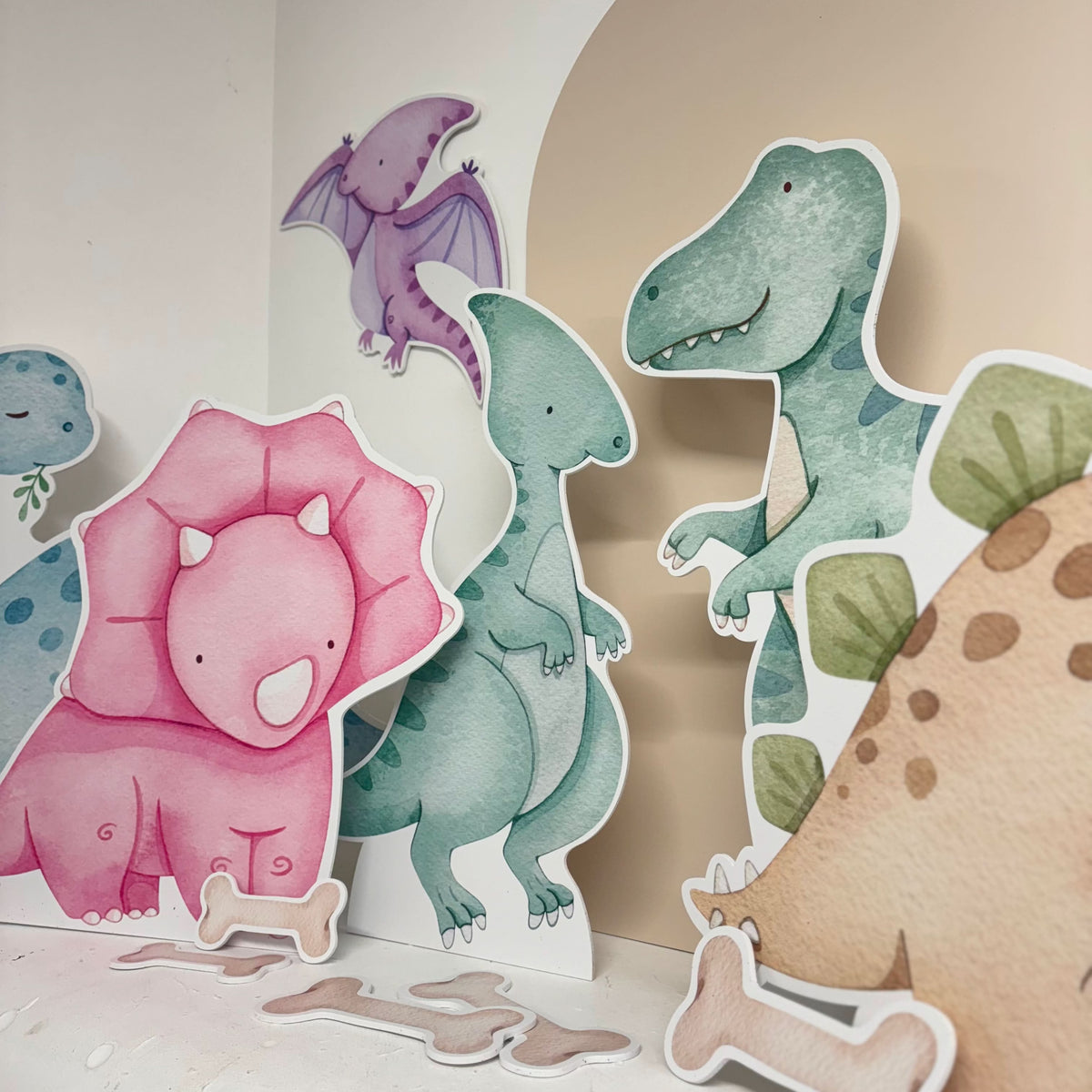 Close-up of Candy Dinos waterproof foamex cutouts showing pink triceratops, blue T-rex, purple pterodactyl, and dinosaur bone and footprint party decorations