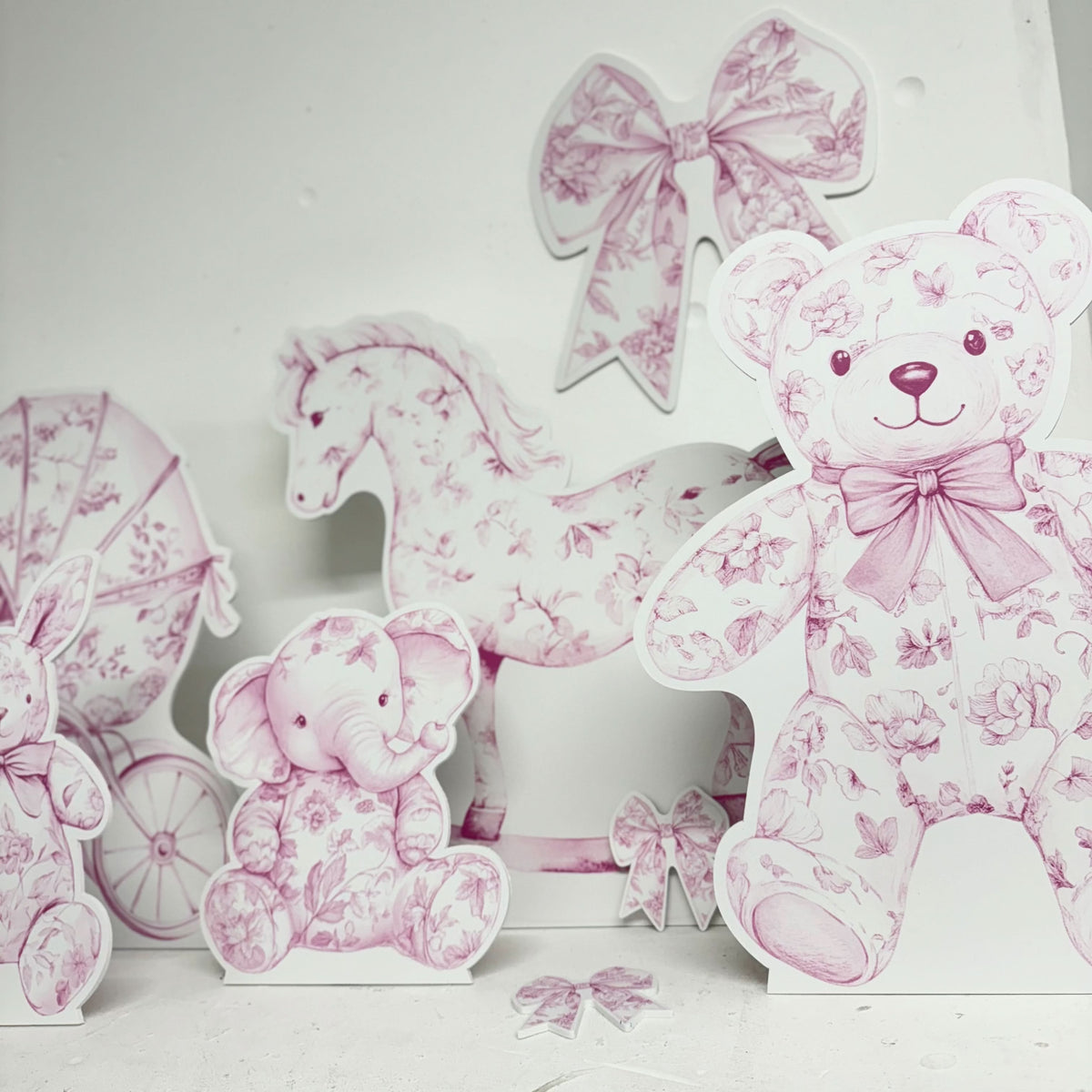 Close-up of Mini Pink Baby Set waterproof foamex cutouts showing pink floral teddy bear with bow, rocking horse, stroller, and baby shower decorations