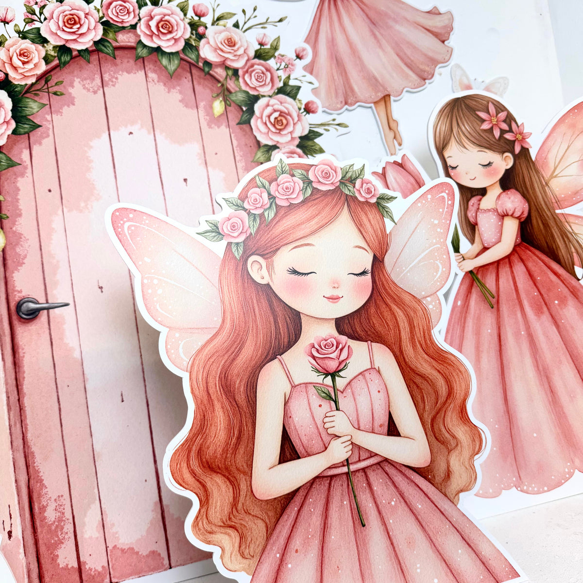 Close-up of Mini Fairytale Princess waterproof foamex cutouts showing fairy holding a rose, pink fairy door with roses, and flying fairy in the background