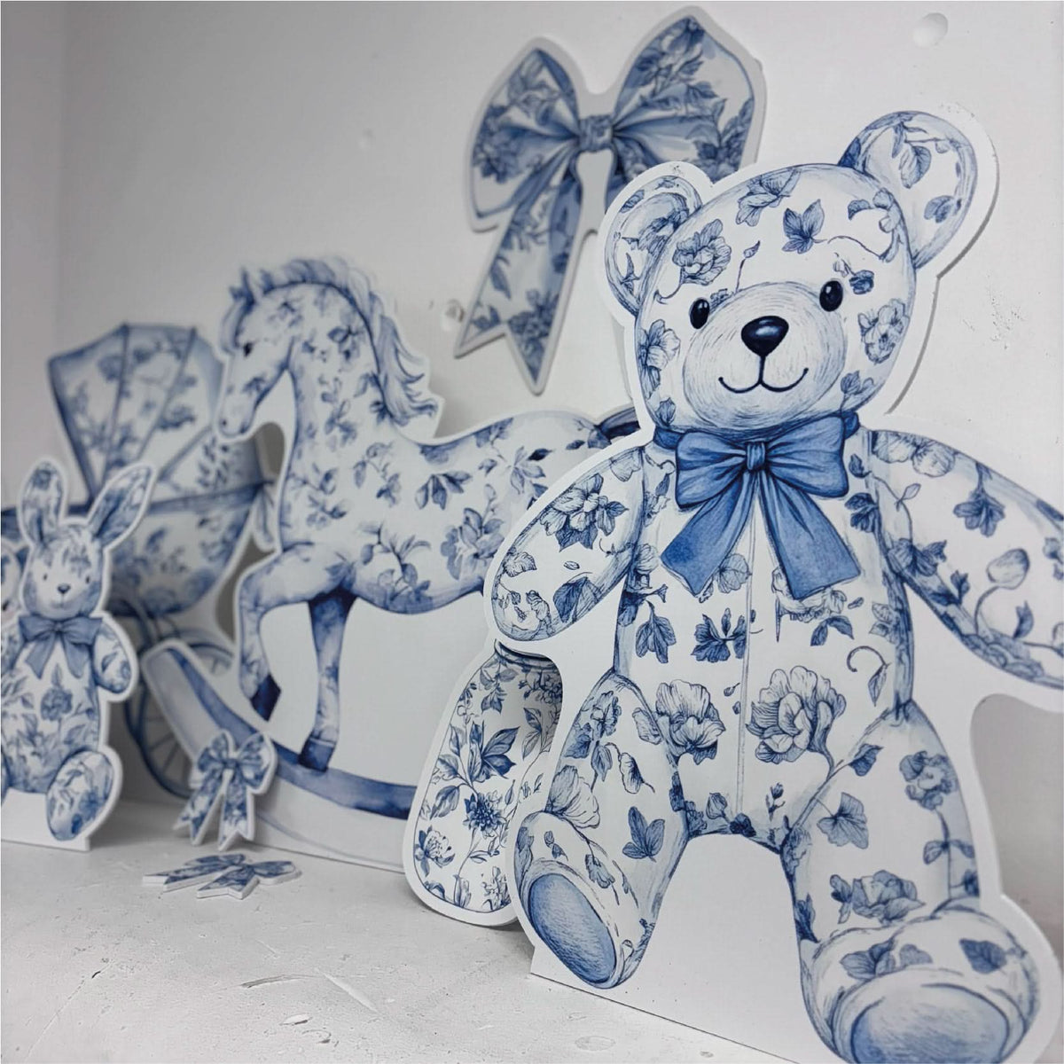 Close-up of Mini Blue Baby Set waterproof foamex cutouts showing blue floral teddy bear with bow, rocking horse, stroller, and baby shower decorations